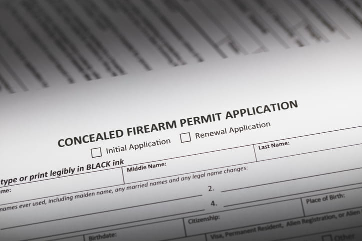 Close-up of a printed Concealed Firearm Permit Application form with checkboxes for initial or renewal application and spaces for personal information.
