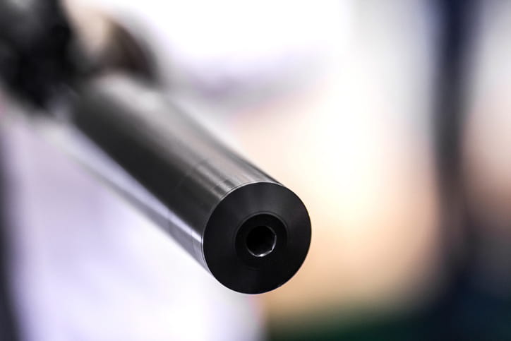 Close-up of a firearm barrel muzzle pointing forward against a soft blurred background, highlighting the precision metalwork of the gun.