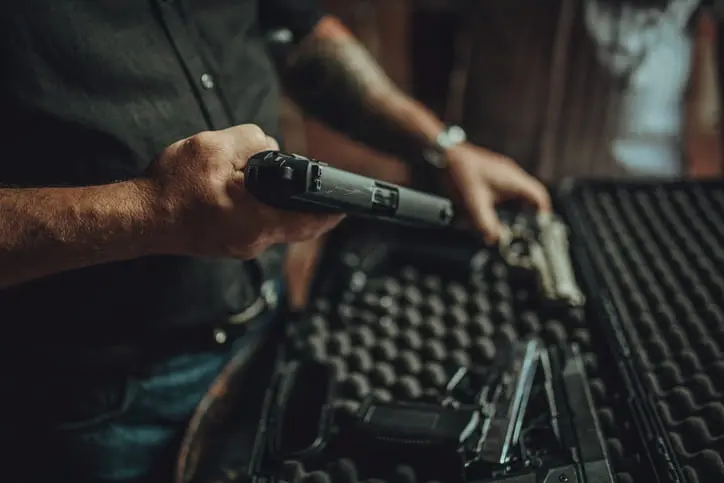 Person placing a handgun into a foam-lined gun case, with another firearm visible inside the case.