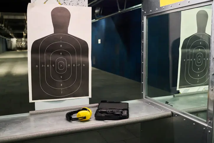 Indoor shooting range lane with a silhouette target, ear protection, and a gun case on the shooting bench